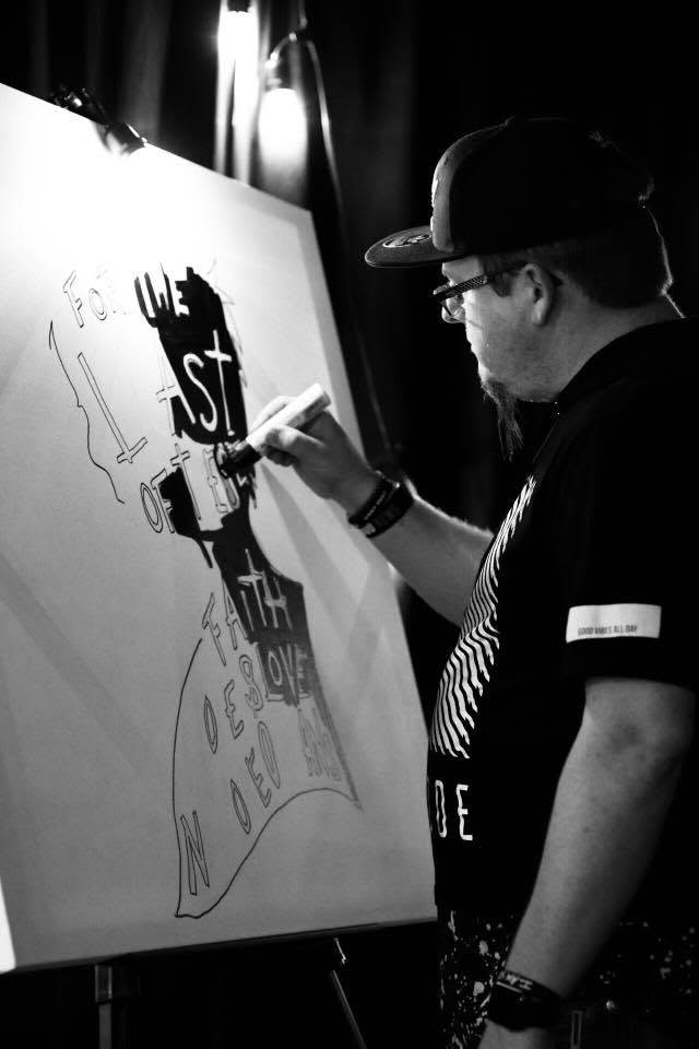 Jim McMahel painting the words For the Least of These on a canvas on stage, black and white