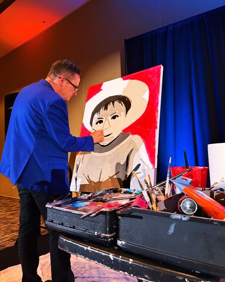 Jim McMahel in a blue blazer painting a portrait of a child in a white hat on stage at a gala
